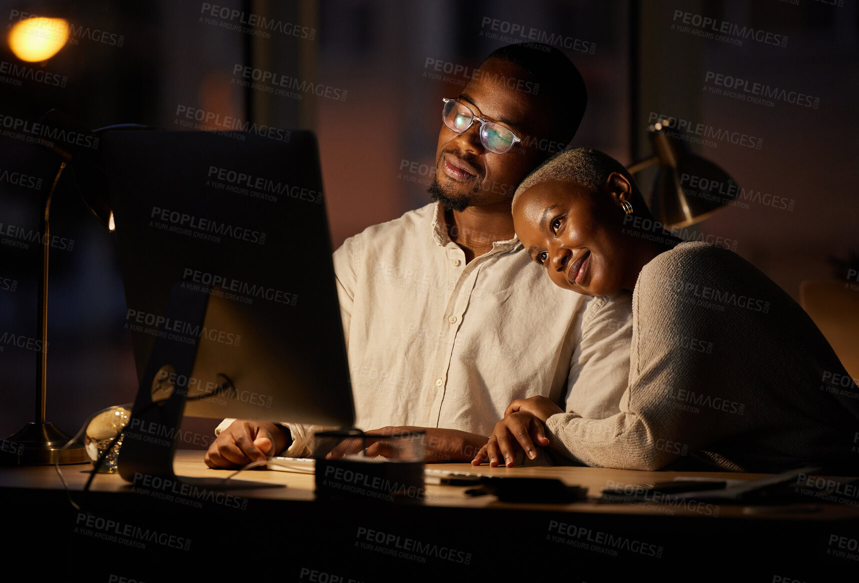 Buy stock photo Shot of two affectionate businesspeople working together on a computer in an office at night