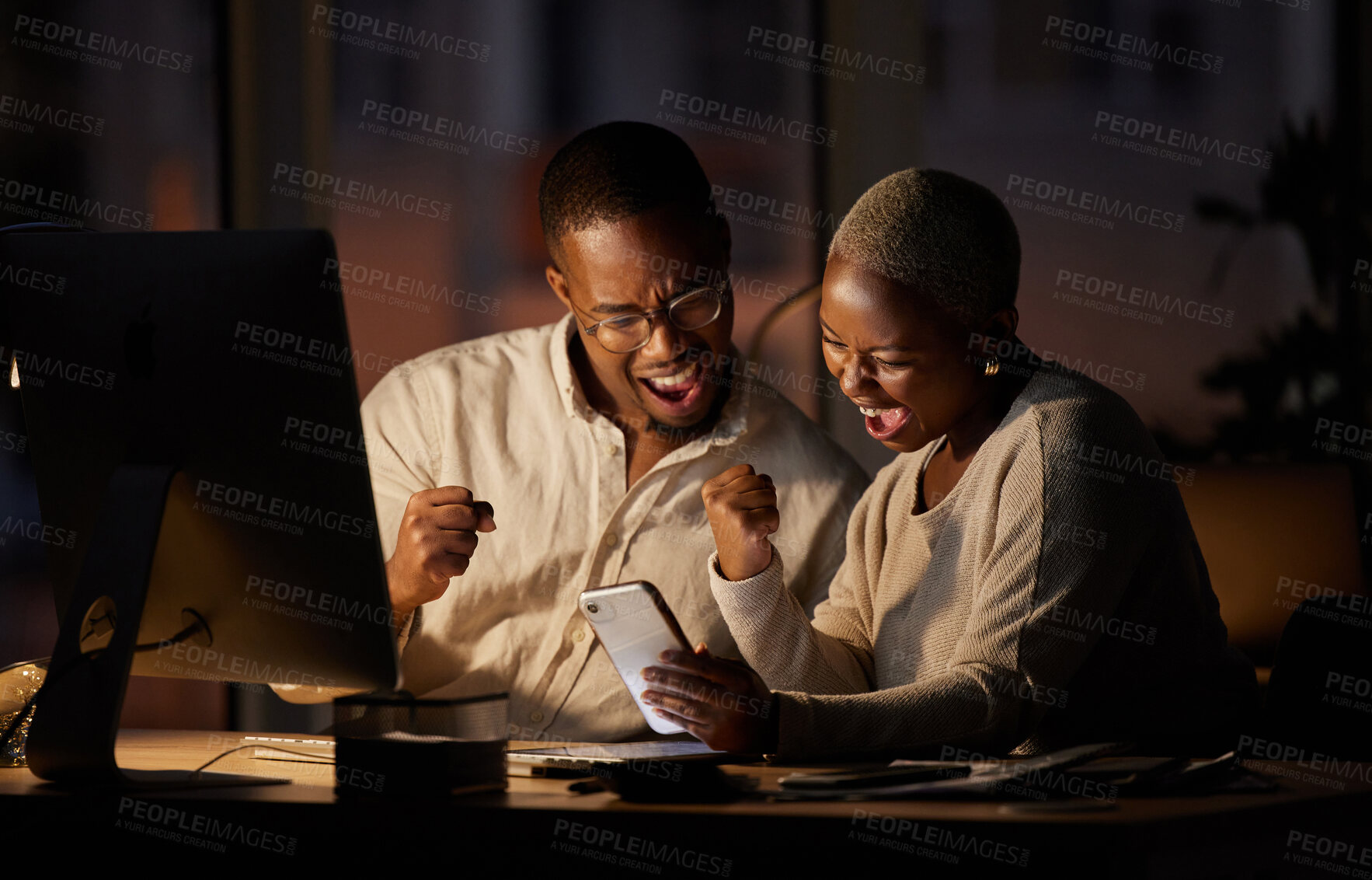 Buy stock photo Shot of two businesspeople cheering while working together in an office at night