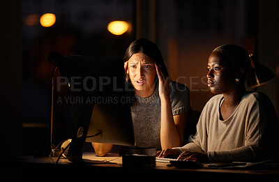 Buy stock photo Shot of two businesswomen looking confused while working together on a computer in an office at night