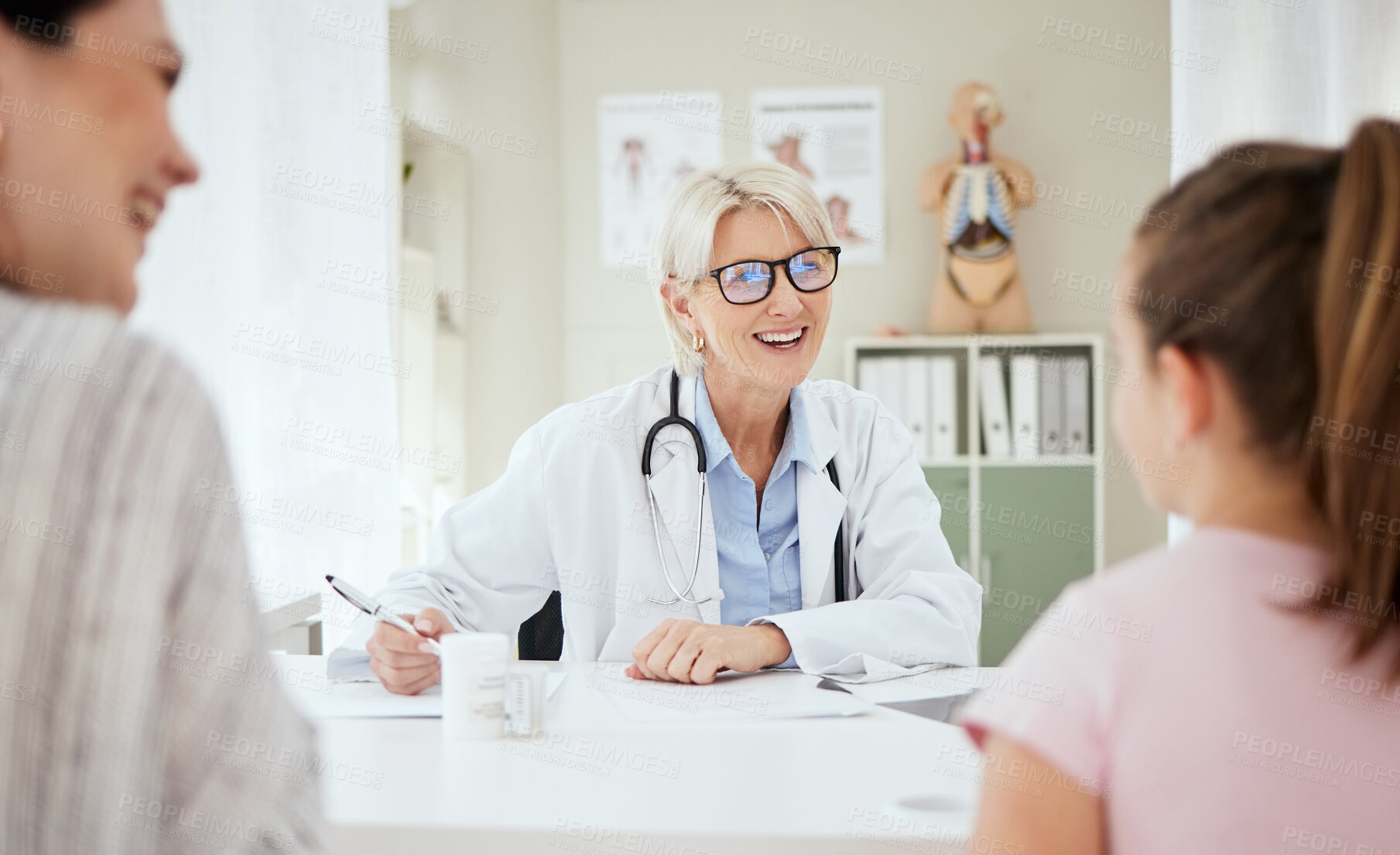 Buy stock photo Checkup, doctor and talking to child, smile and mature woman with question, growth and development. Office, mom and daughter in appointment, writing and conversation for health of kid or pediatrician