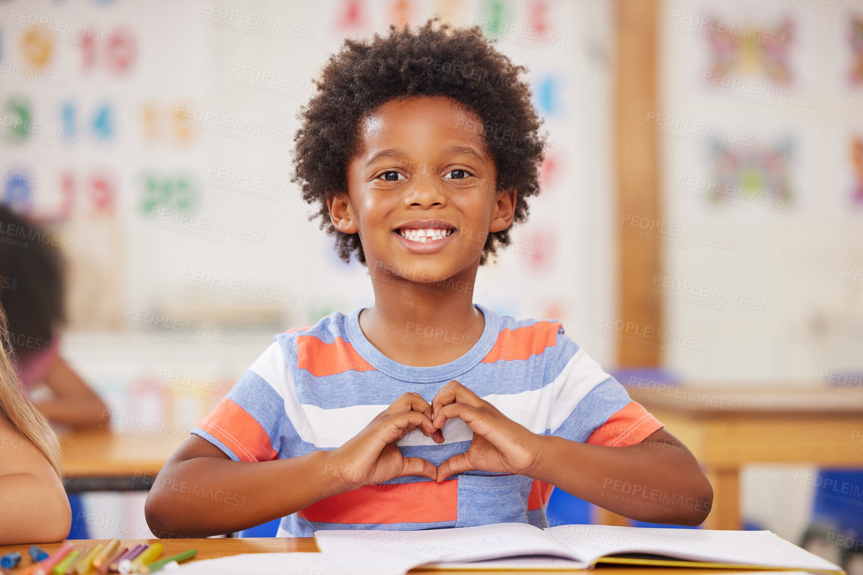 Buy stock photo Shot of a preschool student forming a heart shape with his hands while sitting in class