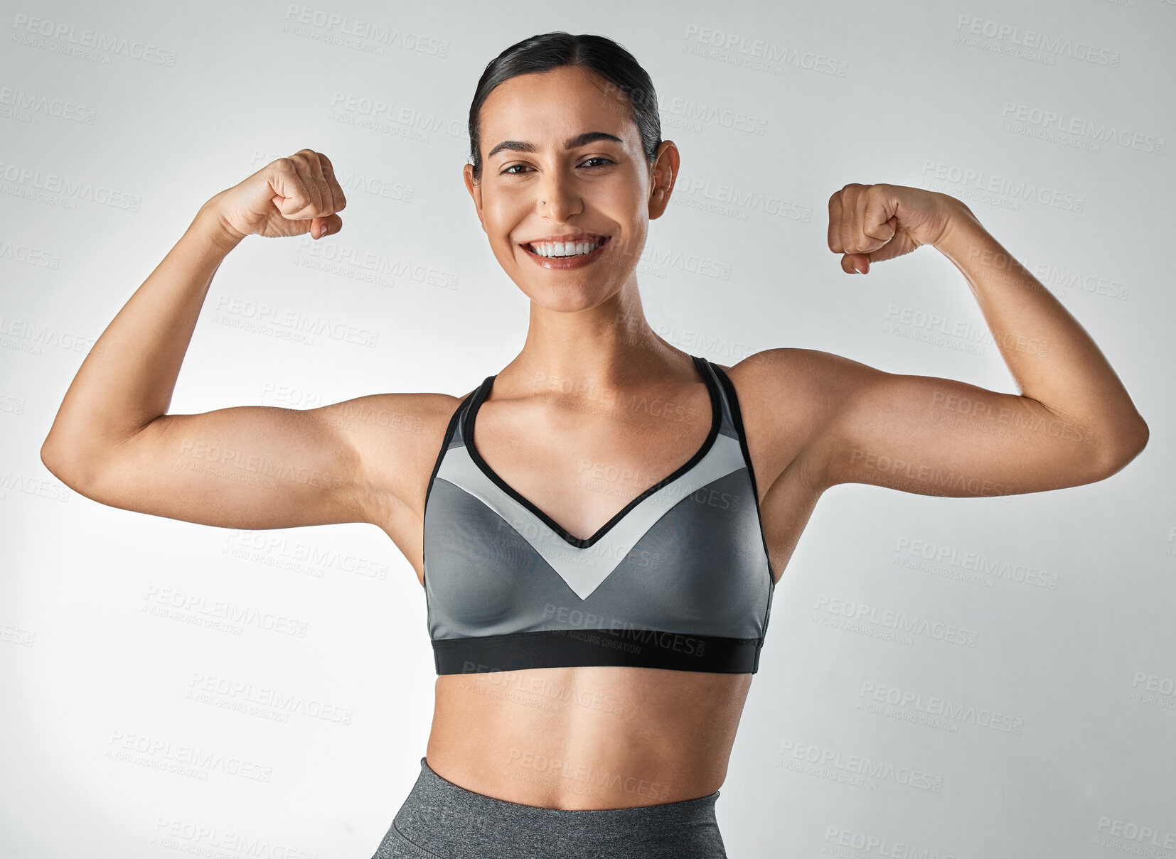 Buy stock photo Studio portrait of a sporty young woman flexing her arms against a grey background