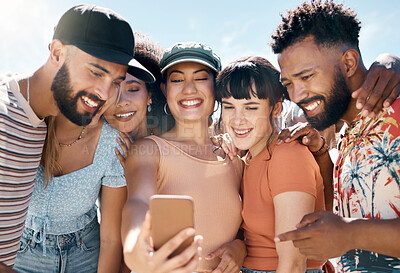 Buy stock photo Shot of a diverse group of friends standing together and using a cellphone to take selfies during a day outdoors