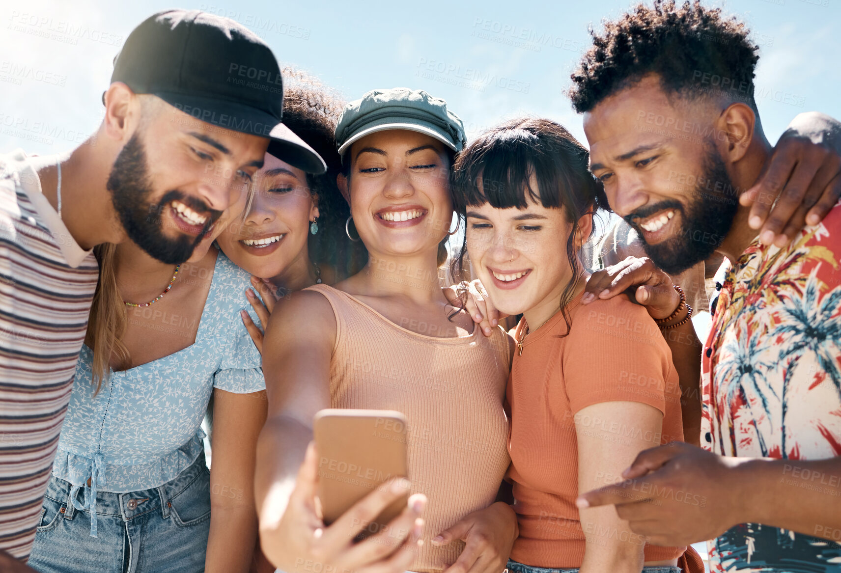 Buy stock photo Shot of a diverse group of friends standing together and using a cellphone to take selfies during a day outdoors