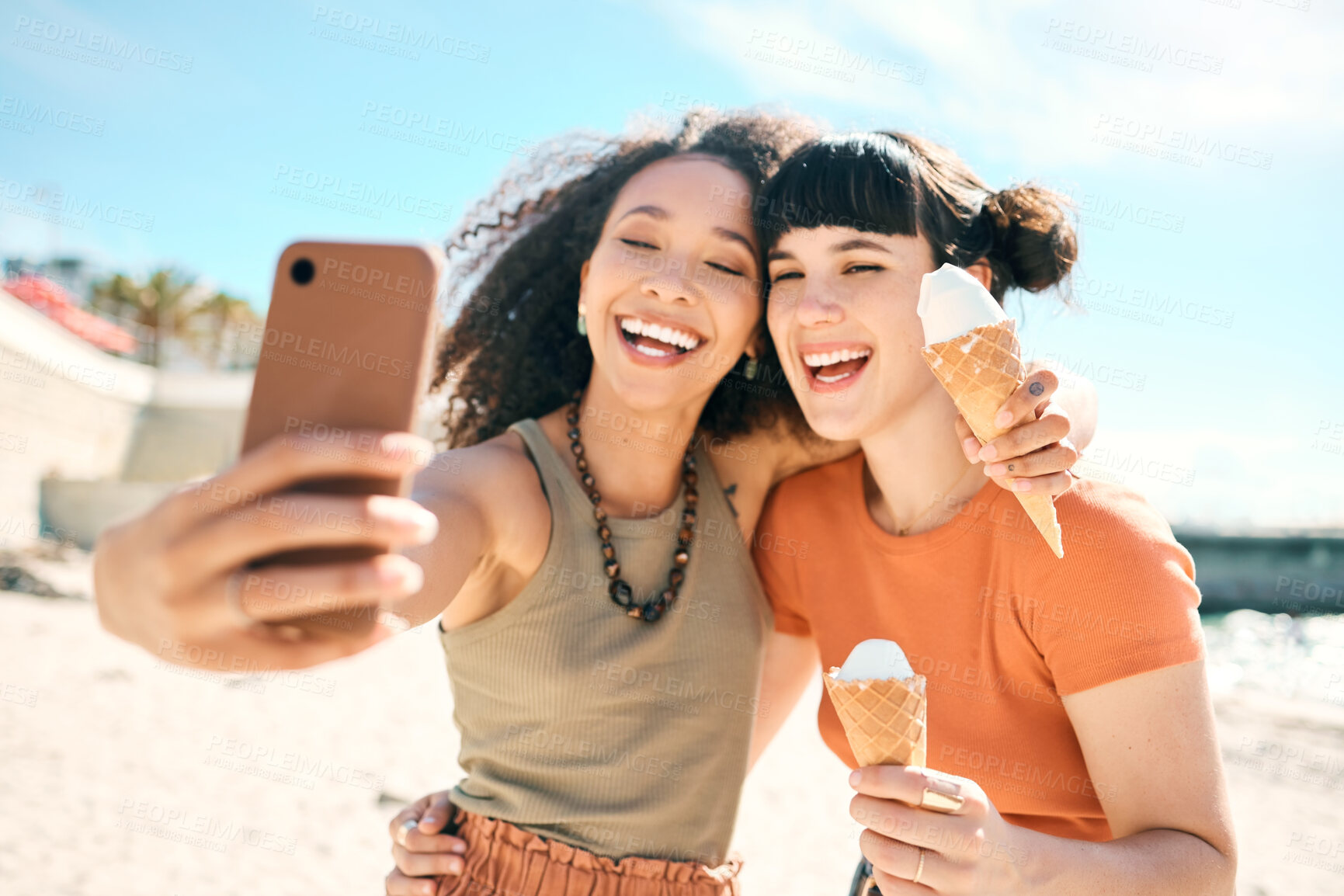 Buy stock photo Cropped shot of two attractive young girlfriends taking selfies while enjoying ice creams on the beach