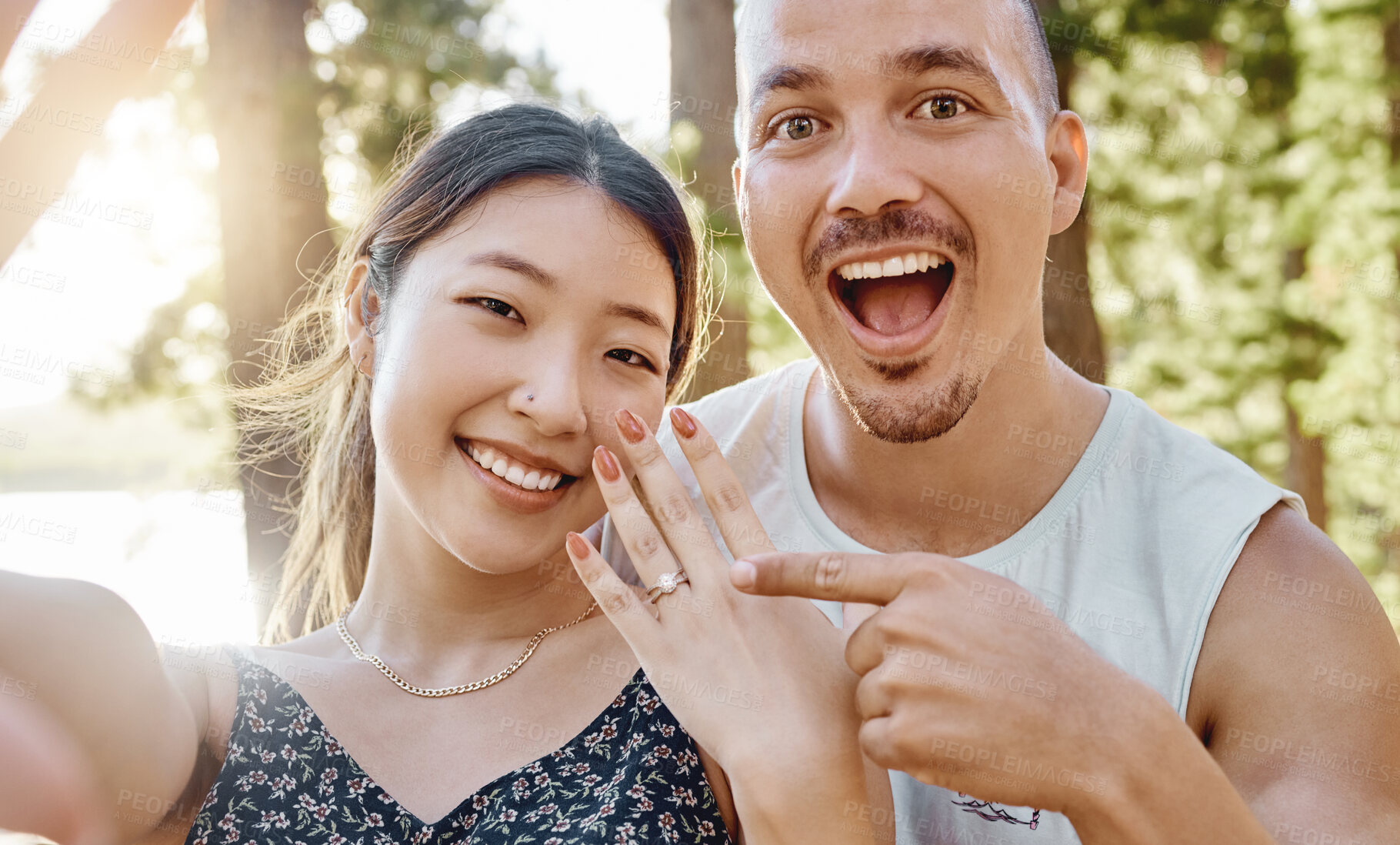 Buy stock photo Couple, engagement and ring in selfie with smile, excited face and pointing for memory in forrest. Young man, happy woman and jewellery for proposal, marriage offer and photography for social network