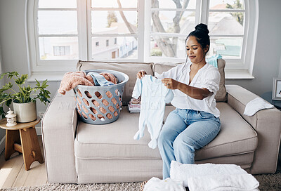 Buy stock photo Shot of an attractive young woman sitting alone in her living room and folding baby clothes