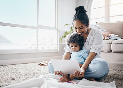 Buy stock photo Full length shot of a young woman sitting in the living room with her daughter and using a digital tablet