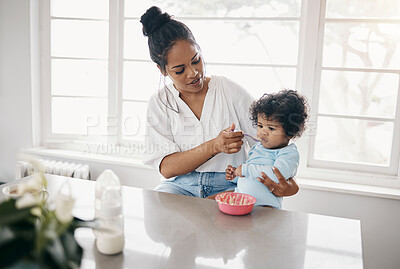 Buy stock photo Shot an attractive young woman sitting in the kitchen with her daughter and feeding her