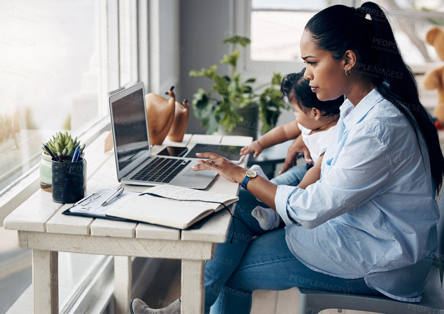 Buy stock photo Shot of a young mother caring for her baby girl while working from home