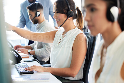 Buy stock photo Shot of an attractive young call centre agent sitting in the office with her colleagues and using her computer