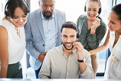Buy stock photo Shot of a young call centre agent sitting in the office while his colleagues watch him