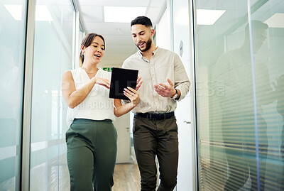 Buy stock photo Shot of two young businesspeople walking through the office together and having a discussion while using a digital tablet