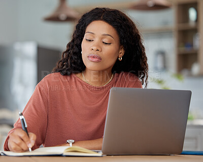 Buy stock photo Shot of a young woman writing notes while working on a laptop at home
