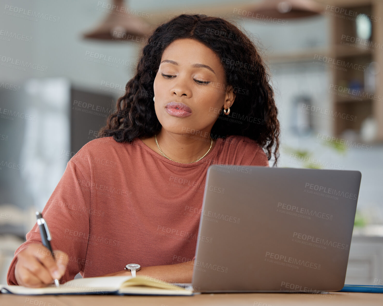 Buy stock photo Shot of a young woman writing notes while working on a laptop at home
