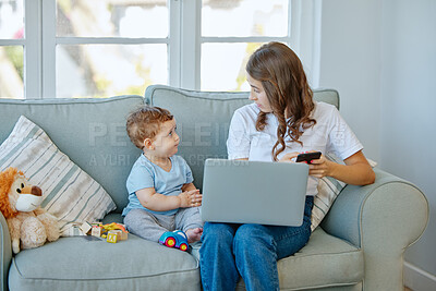 Buy stock photo Cropped shot of an attractive young woman working on her laptop while looking after her baby boy