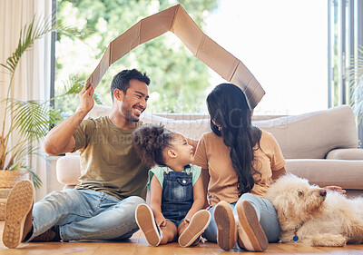 Buy stock photo Full length shot of a handsome young man holding a cardboard box over the heads of himself and his family in their living room at home