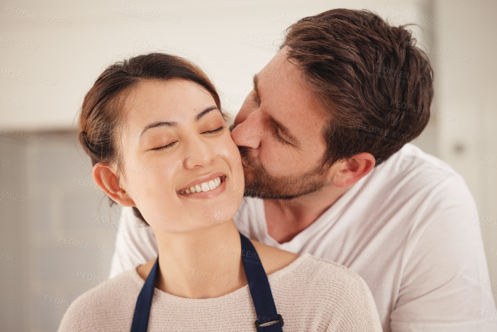 Buy stock photo Happy couple, bonding and embrace with kiss in kitchen at home in together, love and affection as partner. Married people, romantic and anniversary for dinner date in house in celebrating marriage
