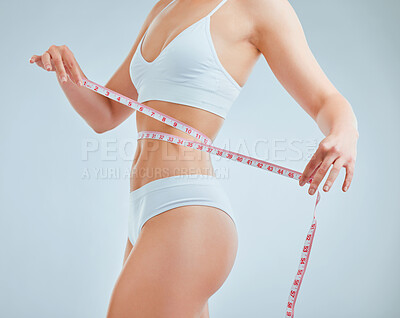 Buy stock photo Cropped shot of a woman holding a measuring tape around her waist