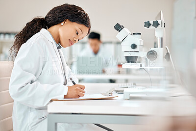 Buy stock photo Shot of a young scientist writing notes while using a microscope in a lab