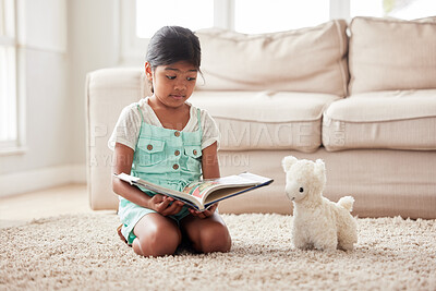 Girl playing pretend and reading a book to her toy while sitting on the floor at home and learning
