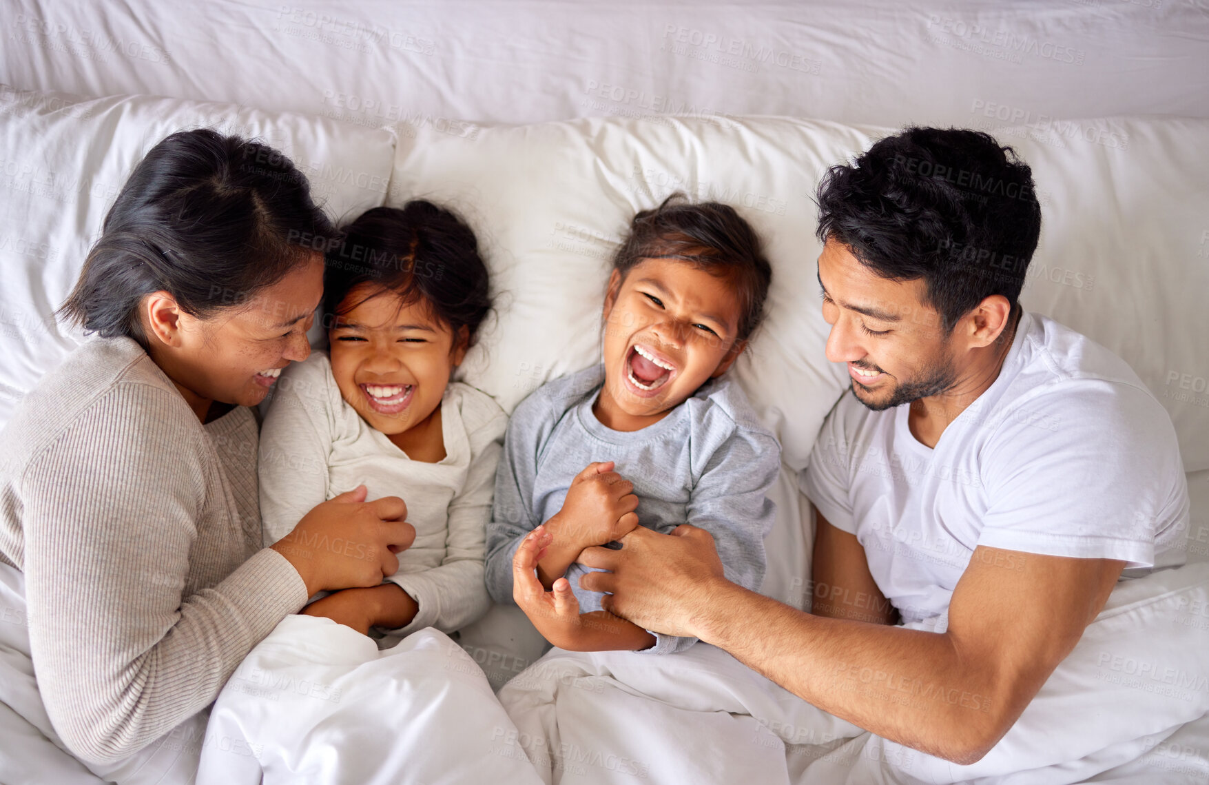 Buy stock photo Family, tickle and laughing on bed together, love and bonding for security in relationship. Parents, children and above for kids or support on weekend, play and morning happiness in bedroom of home