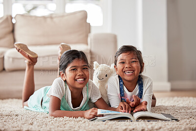 Little sisters happily practicing their reading while lying on the lounge floor together at home during lockdown