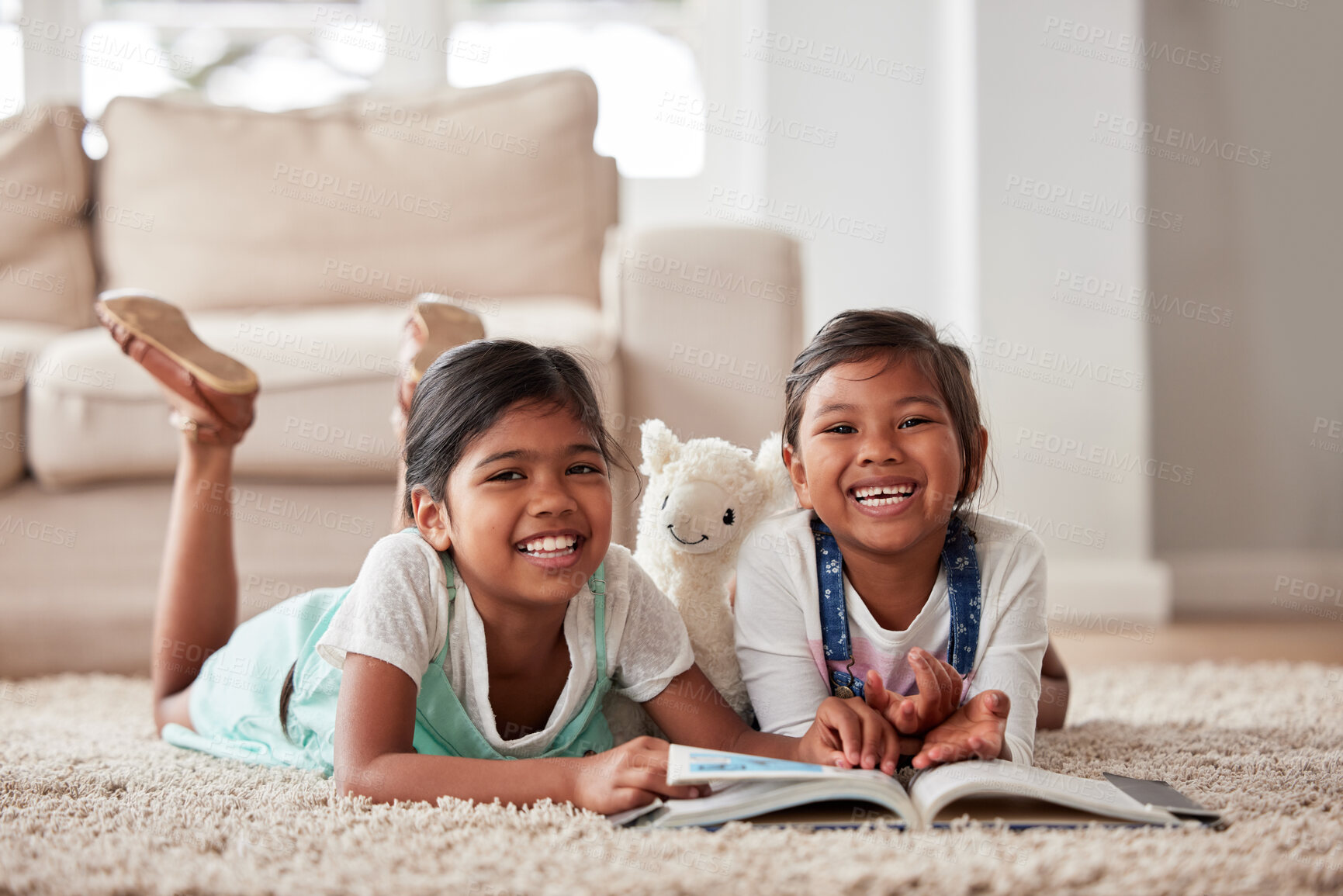 Buy stock photo Little sisters happily practicing their reading while lying on the lounge floor together at home during lockdown