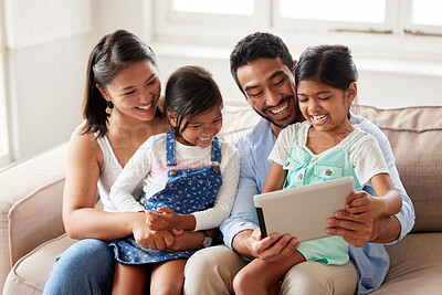Happy ethnic family of four sitting on the couch together using a digital tablet while streaming and looking happy