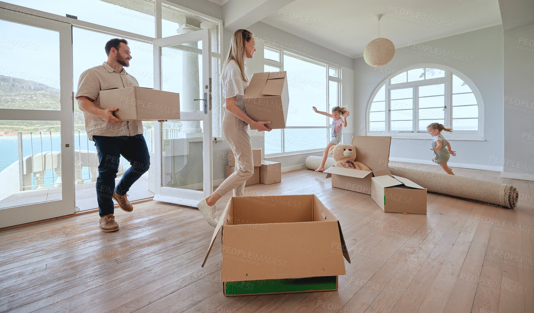 Buy stock photo Excited children, parents and new home with boxes for moving in, mortgage and real estate in living room. Happy family, people and kids play on carpet or running for property in California by beach