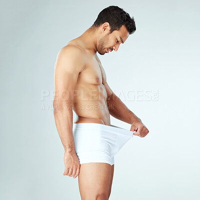 Buy stock photo Shot of a young man checking his private parts against a studio background