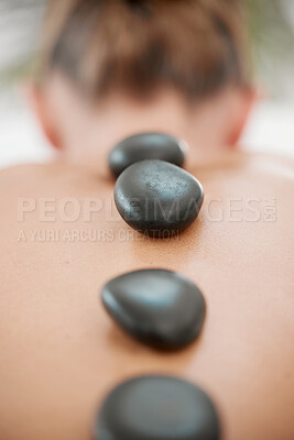 Buy stock photo Spa, calm and woman with rocks for massage, luxury treatment or stress relief on bed. Rear view, relax and female person with hot stones for back therapy, muscle tension or healing body at resort