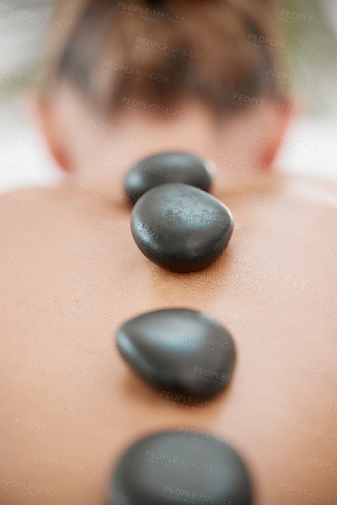 Buy stock photo Spa, calm and woman with rocks for massage, luxury treatment or stress relief on bed. Rear view, relax and female person with hot stones for back therapy, muscle tension or healing body at resort