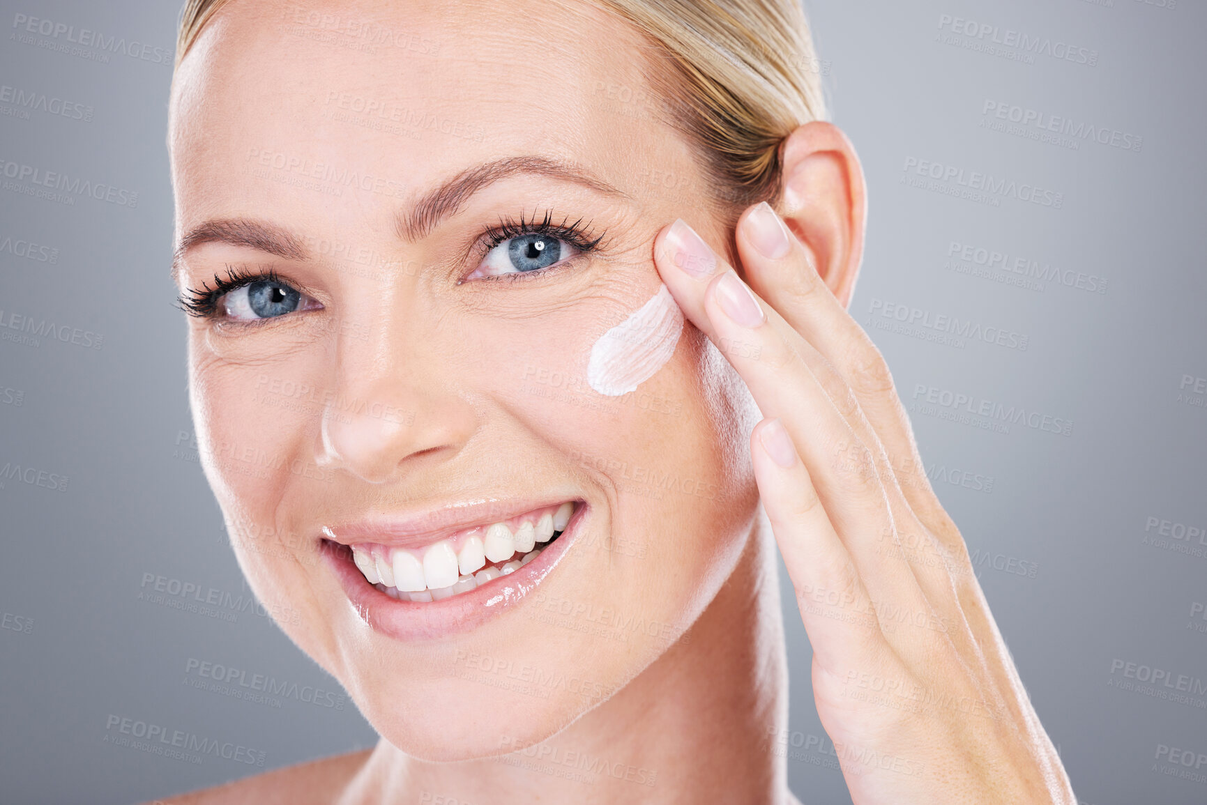 Buy stock photo Studio portrait of an attractive mature woman applying moisturiser on her face against a grey background