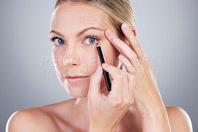 Buy stock photo Studio portrait of an attractive mature woman applying eyeliner against a grey background