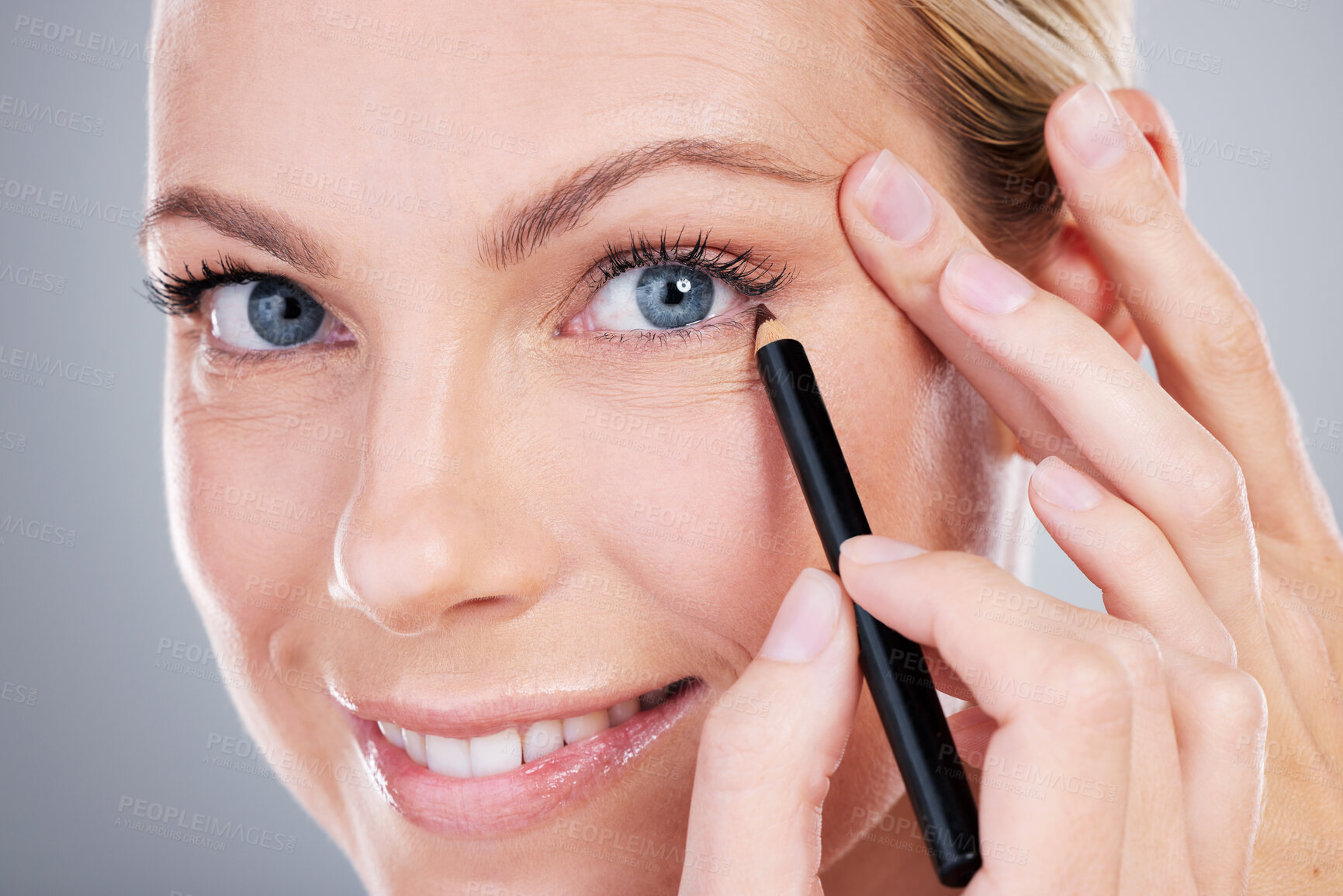 Buy stock photo Studio portrait of an attractive mature woman applying eyeliner against a grey background