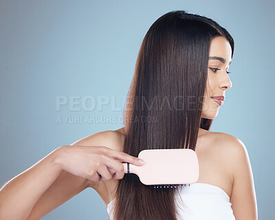 Buy stock photo Studio shot of a beautiful young woman brushing her long silky hair while posing against a blue background