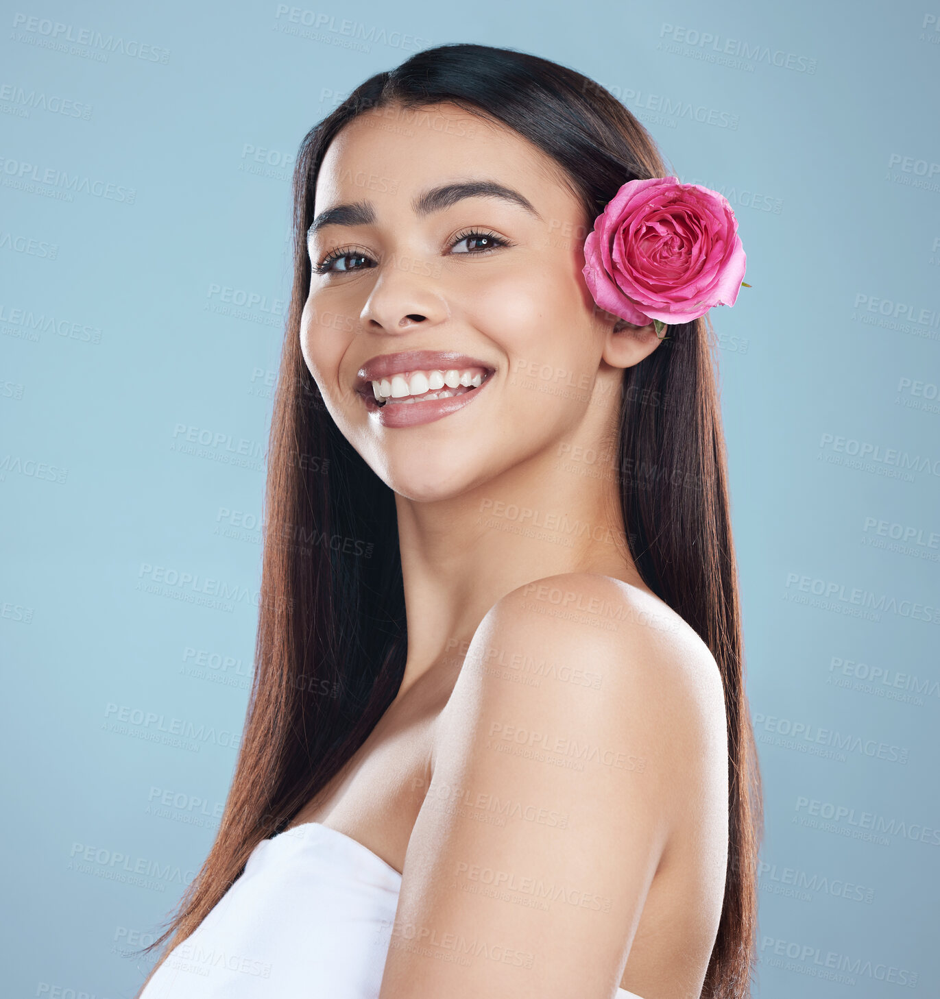 Buy stock photo Studio portrait of a beautiful young woman wearing a flower in her hair while posing against a blue background