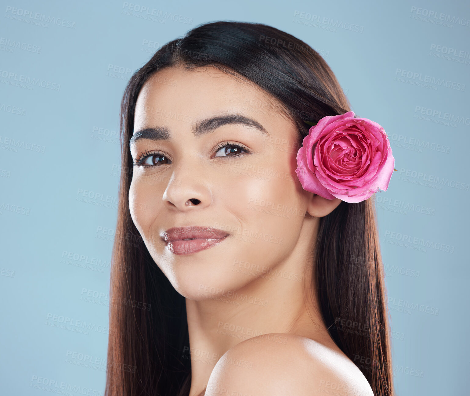 Buy stock photo Studio portrait of a beautiful young woman wearing a flower in her hair while posing against a blue background