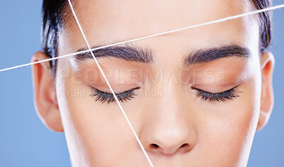 Buy stock photo Cropped shot of an unrecognisable woman posing alone against a blue background in the studio and threading her eyebrows