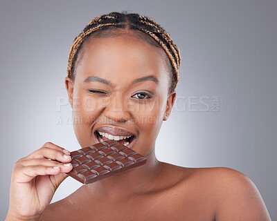 Buy stock photo Black woman, portrait and eating a dark chocolate in studio with skincare, beauty and antioxidants. Model, person and slab candy for cheat meal, sweet craving or wink for snack on gray background