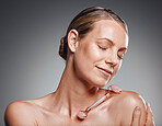 Beautiful mature woman posing with face roller in studio against a grey background