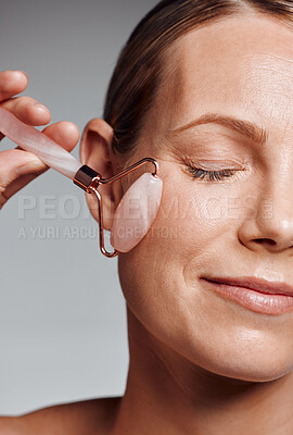 Buy stock photo Beautiful mature woman posing with face roller in studio against a grey background