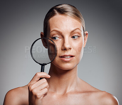 Buy stock photo Beautiful mature woman posing with magnifying glass in studio against a grey background
