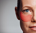Beautiful mature woman posing with under eye patch in studio against a grey background