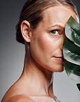 Beautiful mature woman posing with palm leaf in studio against a grey background