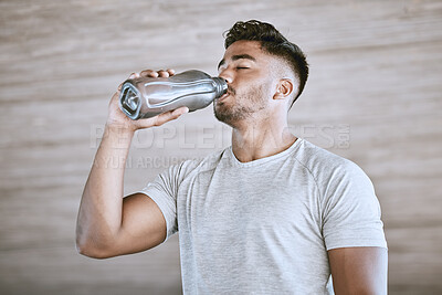 Fit young man drinking water from a bottle while exercising outdoors. Cooling down with a sip of water after training hard
