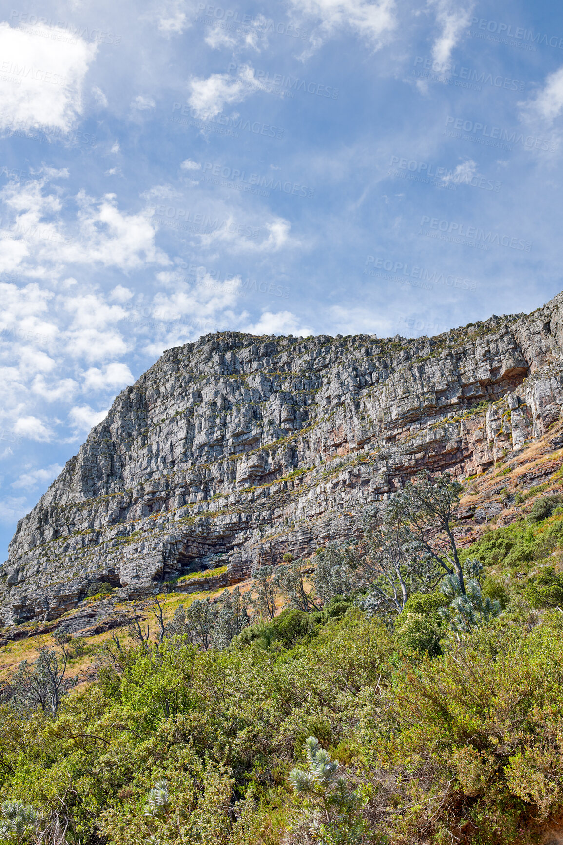 Buy stock photo A big rocky mountain against a blue sky background on a beautiful summer day. Hill with lush green grass and plants growing with the view of clouds in the sky in nature with a natural environment 