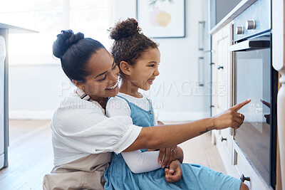 Happy young loving mother and her daughter baking together and having fun while sitting by the oven and watching their homemade cake or cookies bake