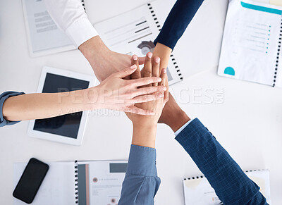 Above view of diverse group of unknown business people huddled over paperwork and stacking their hands in the middle. Team of professionals feeling motivated after meeting and planning a strategy